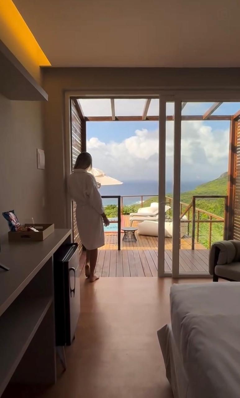 Hóspede em roupão observa o mar a partir de um quarto de pousada em Fernando de Noronha